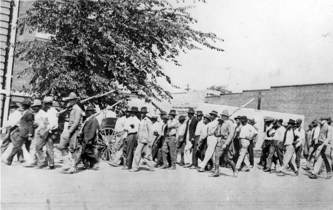 En grupp nationalgardetrupper, som bär gevär med bajonetter fästa, eskorterar obeväpnade svarta män till ett interneringscenter efter Tulsa Race Massacre, Tulsa, Oklahoma, juni 1921.
