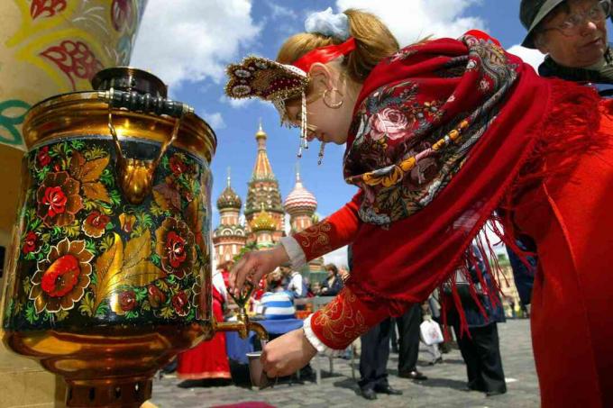 Rysk flicka som bär traditionella kläder häller vatten ur samovar