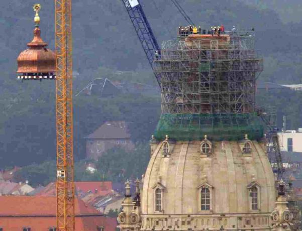 En kran lyfter kopparkupolen och det gyllene korset till toppen av den rekonstruerade Frauenkirche i Dresden, Tyskland