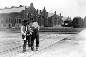 Två tjänstemän står bredvid Pullman Building och tågbilar med låsta armar och en flaska sprit under Chicago Pullman Strike 1894