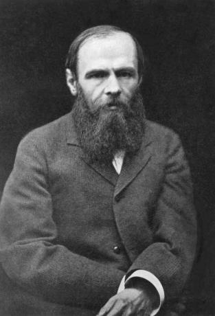Svartvitt fotografi av Dostojevskij, skäggigt och klädd i en kappa