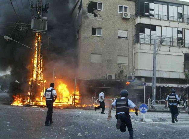 Israeliska poliser rusar till platsen för en brinnande elpylon och skadade byggnadsstunder efter att en volley av Hizbollah-raketer träffade den 13 juli 2006 i den norra staden Nahariya, Israel.