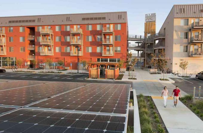 Två personer som går nära gröna byggnader och solpaneler, i en Zero Net Energy-gemenskap